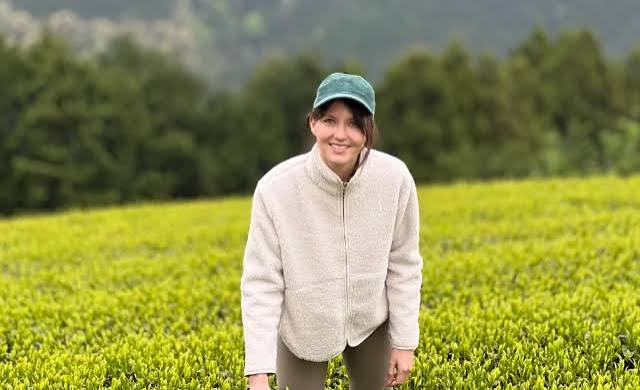 Jeune femme souriante dans une casquette verte, au milieu d'un champ verdoyant.
