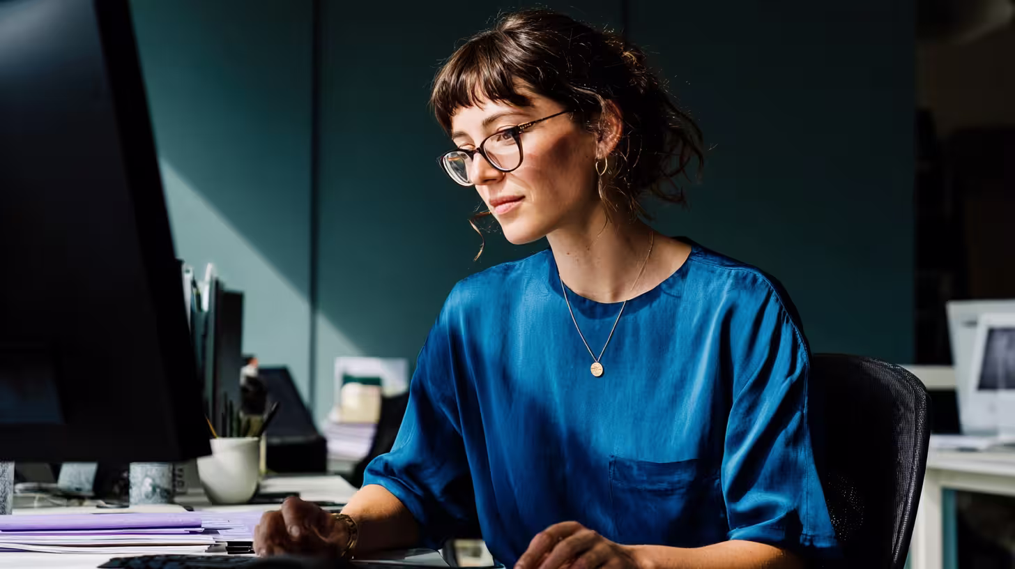 Woman with glasses writing a cold prospecting email at her office computer