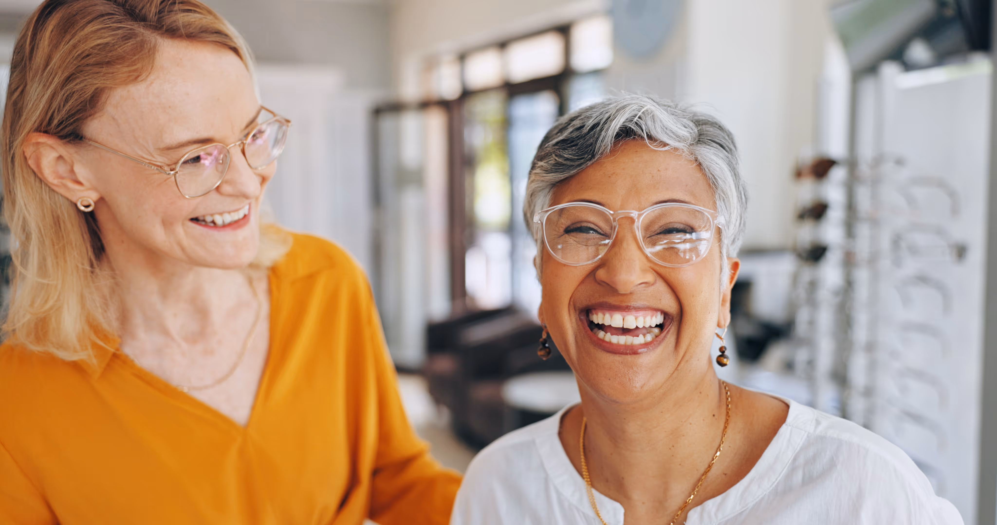 Two women in glasses laughing together in a bright office space