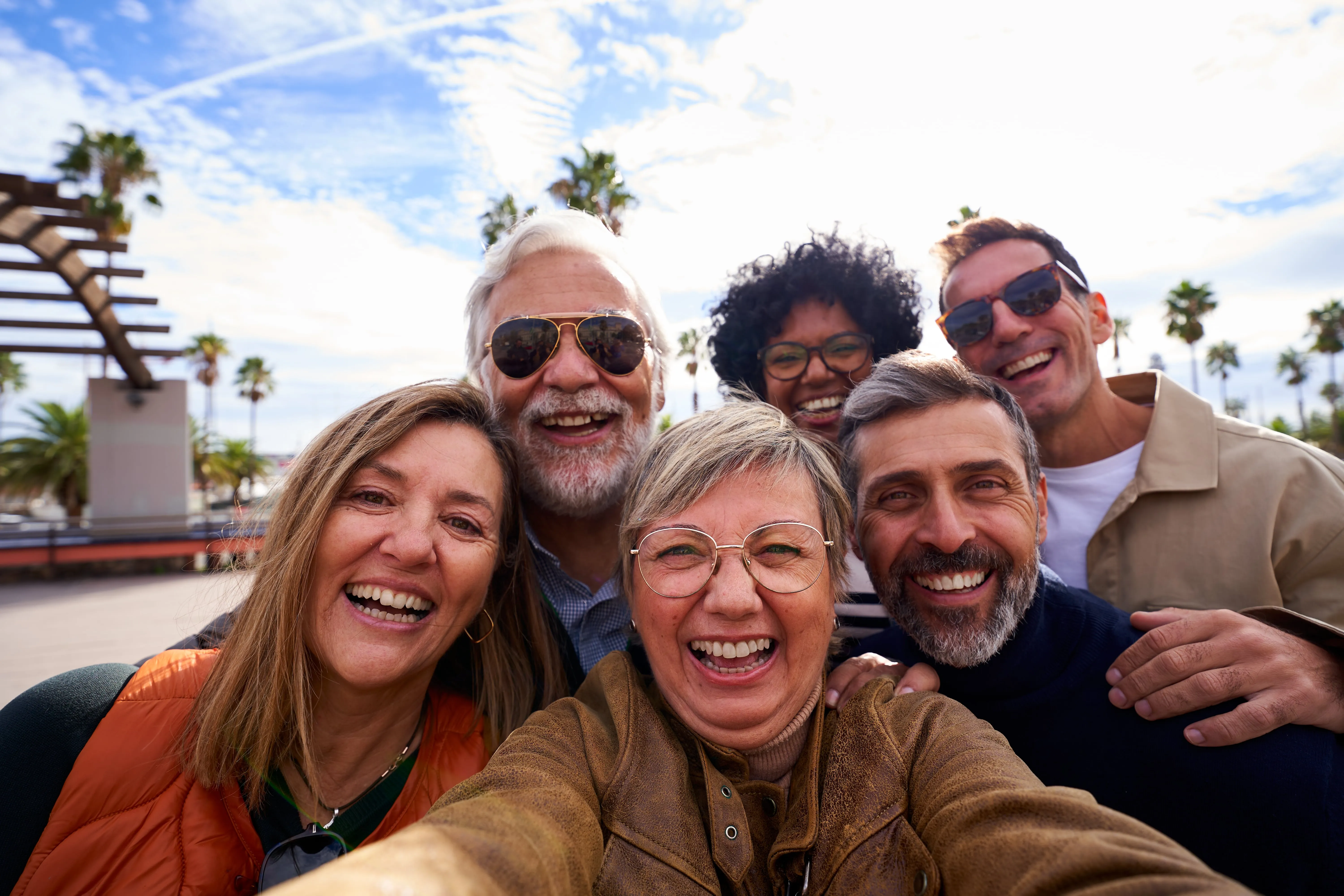 Group of six middle-aged friends laughing together under palm trees