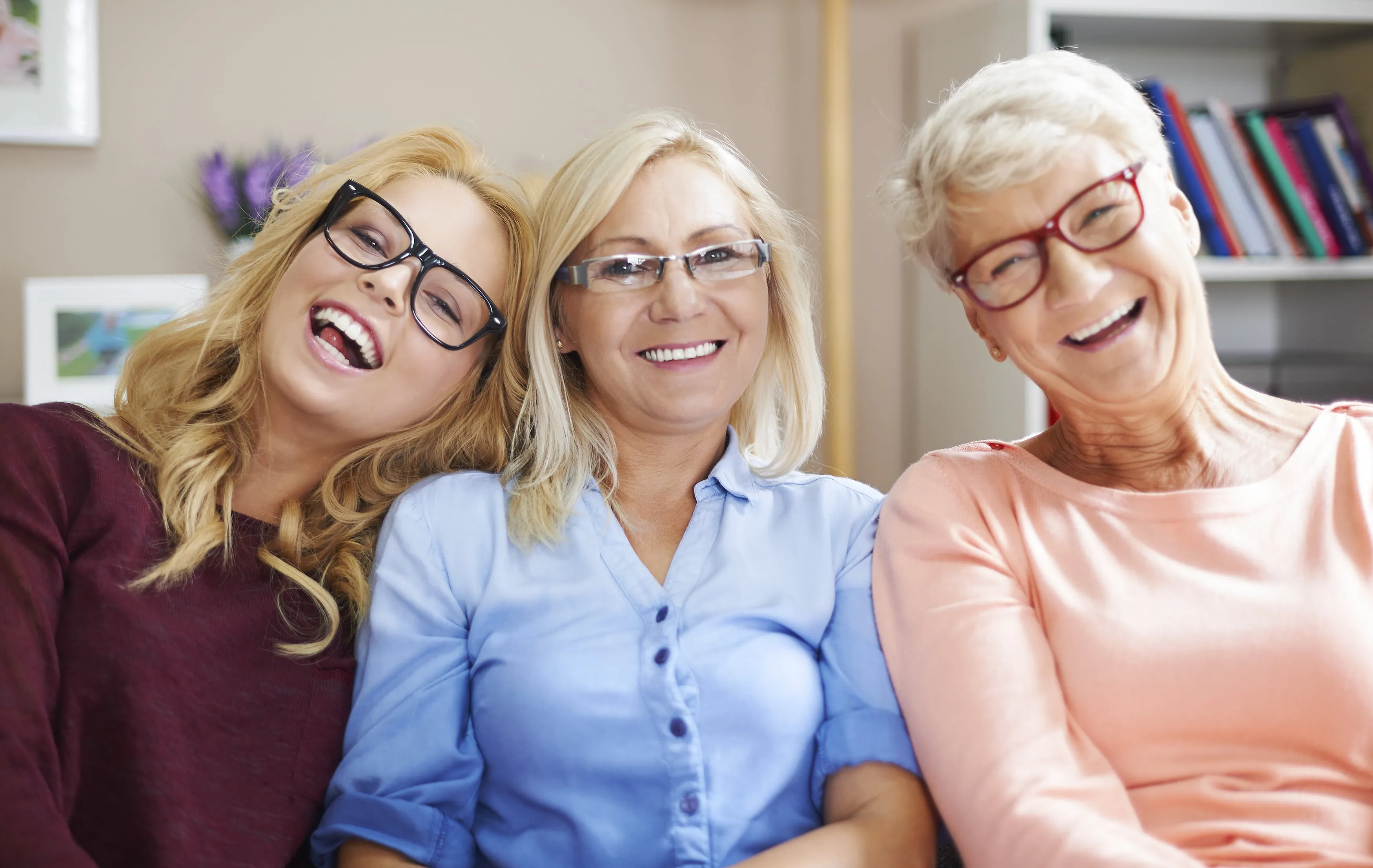 Three women of different ages laughing together, wearing glasses