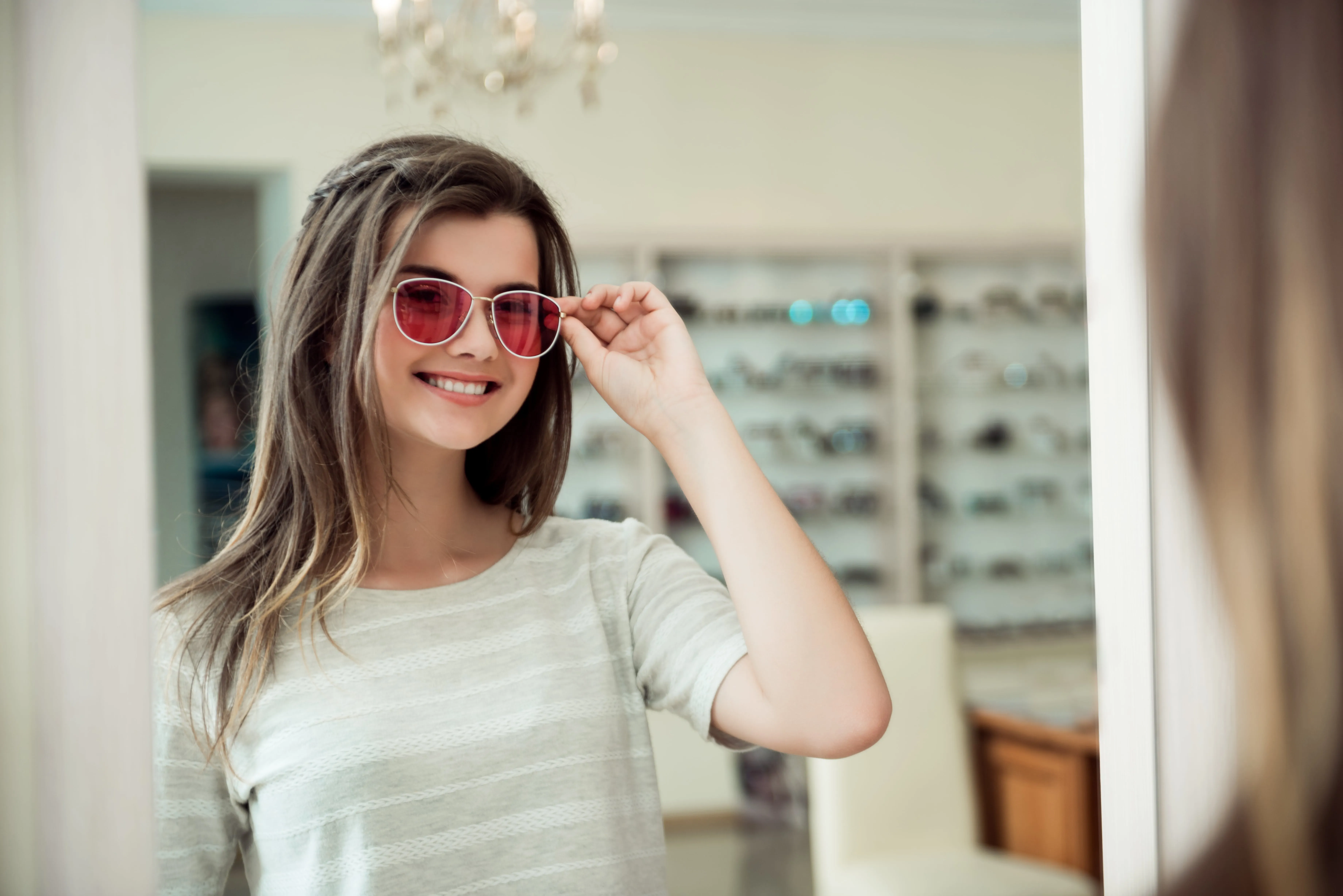 Smiling person wearing red-tinted sunglasses in an eyewear store