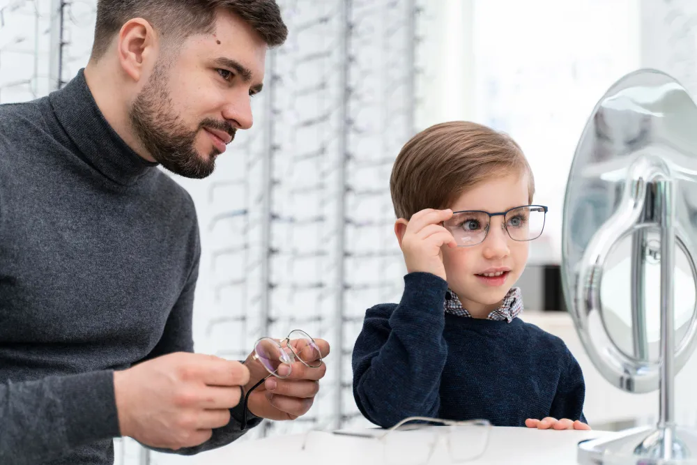 Child trying on glasses with help from adult in optical store