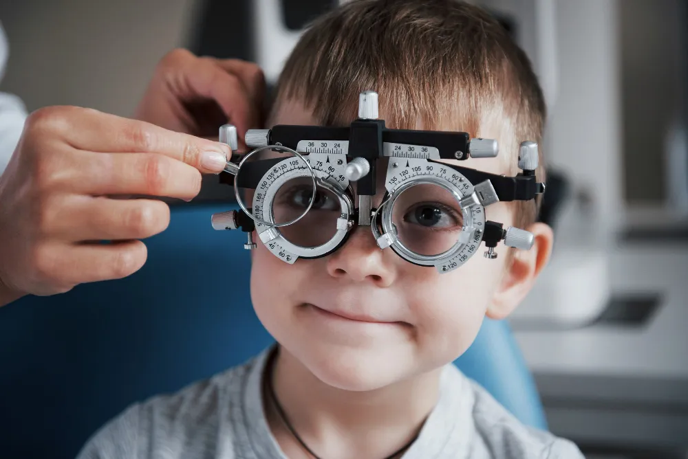 Child wearing trial frame during eye exam, smiling brightly
