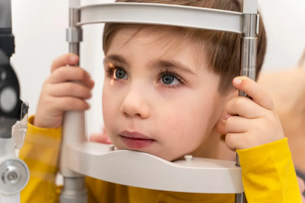 Child getting eye exam with optometry equipment, wearing yellow shirt