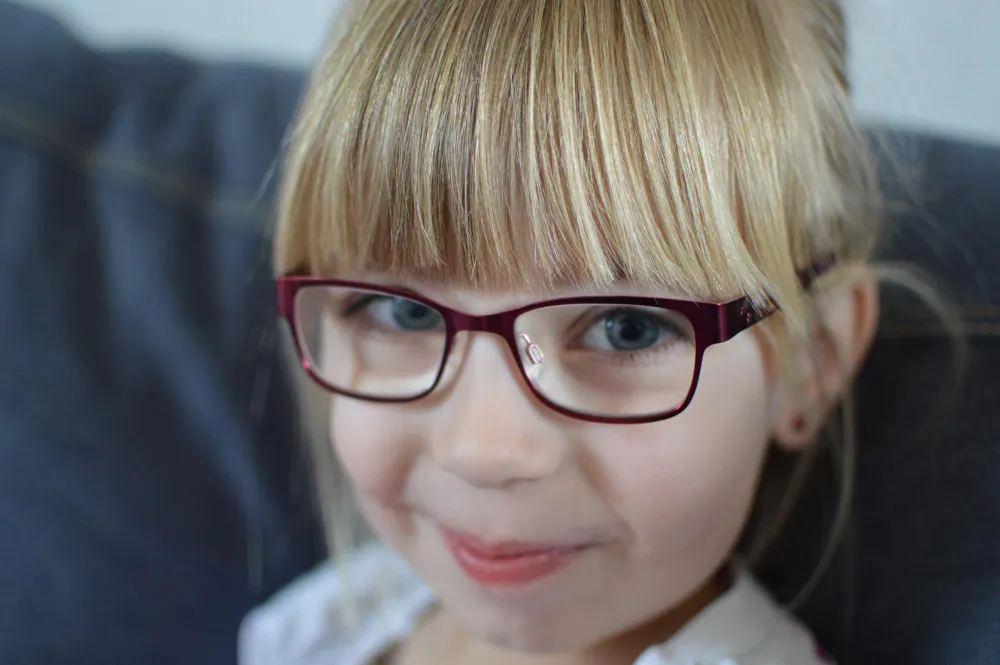 Young child with blonde hair and red glasses smiling softly