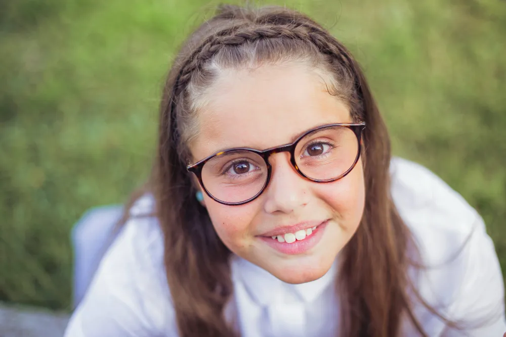 Young student with braided hair and glasses smiling outdoors