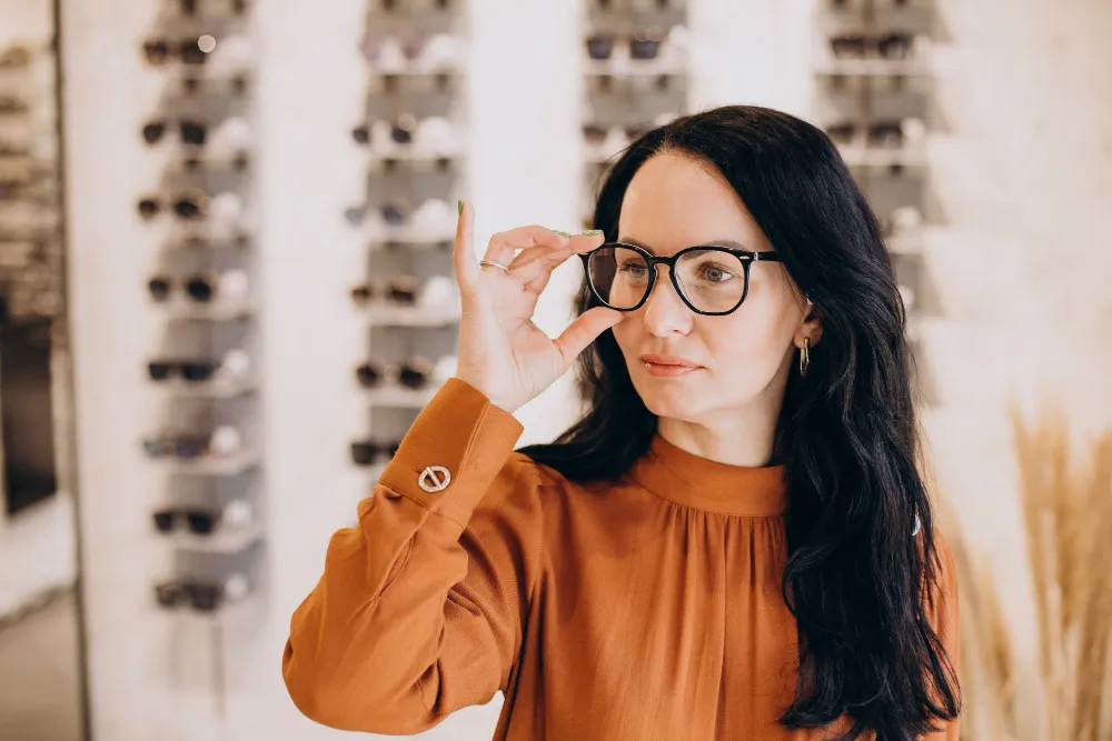 Woman in orange top trying on glasses in eyewear store