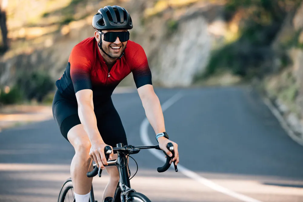 Cyclist in red jersey smiling while riding bike on mountain road