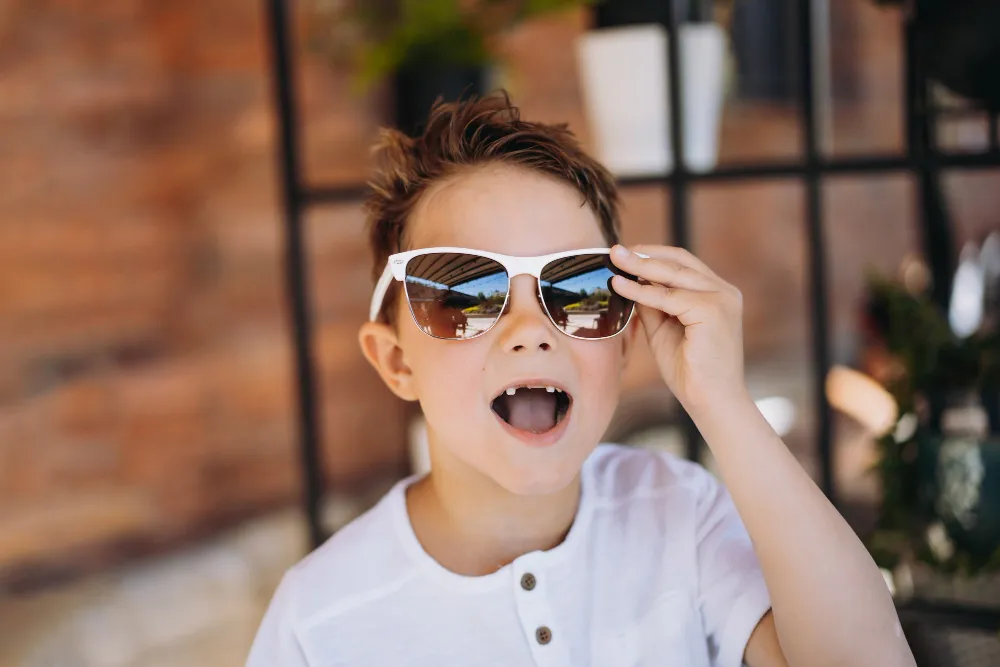 Excited child wearing sunglasses with landscape reflection, adjusting shades