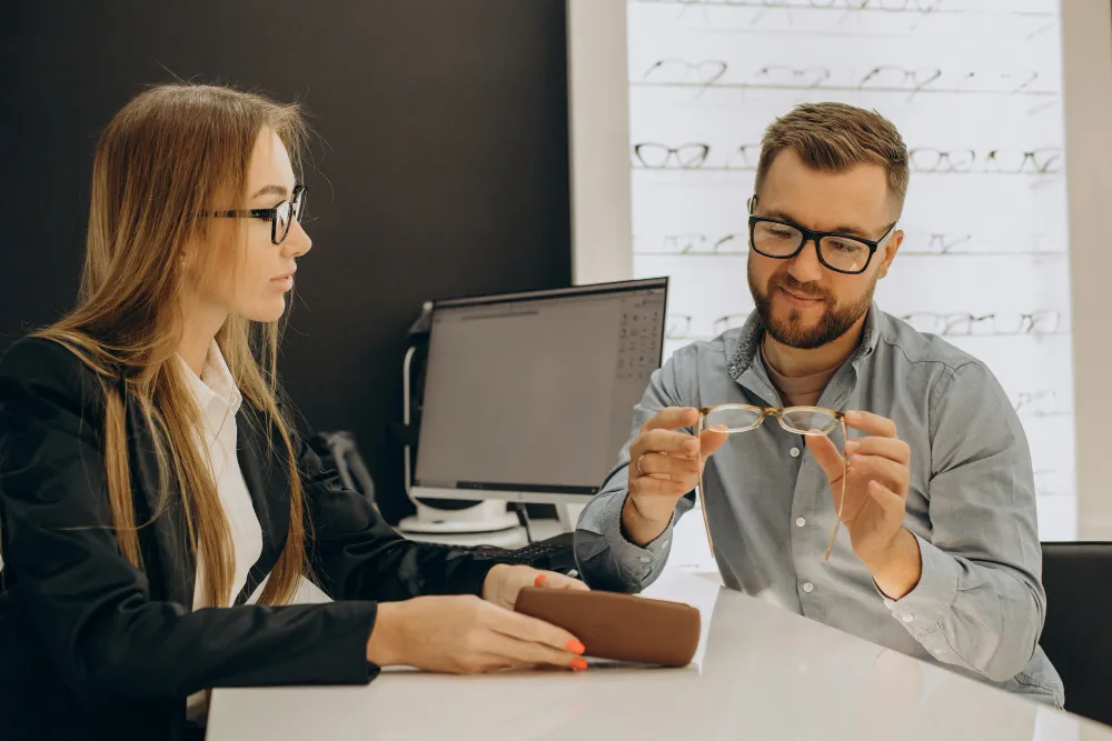 Two professionals discussing eyewear in an office with computer and whiteboard