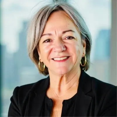 Smiling middle-aged woman with short gray hair wearing gold hoop earrings and a black blazer.