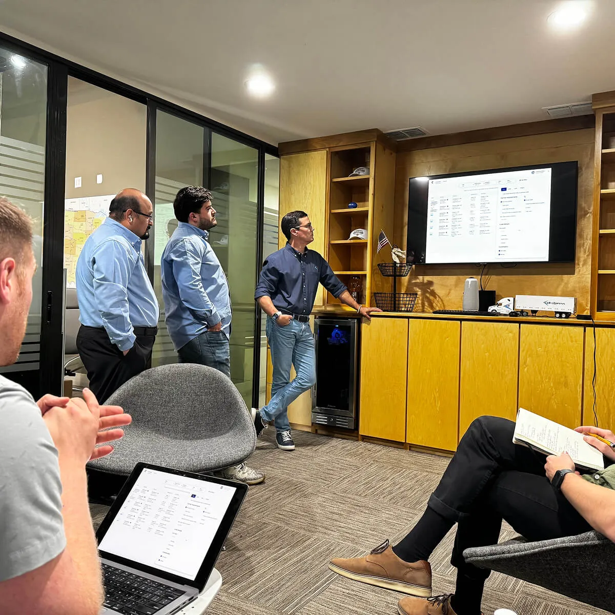Cargado employees in a meeting room viewing a screen and laptops showing data or schedules.