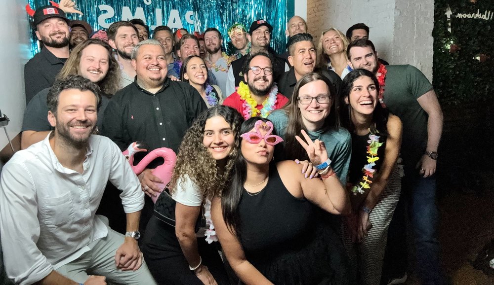 The team in leis and party glasses at a photo booth