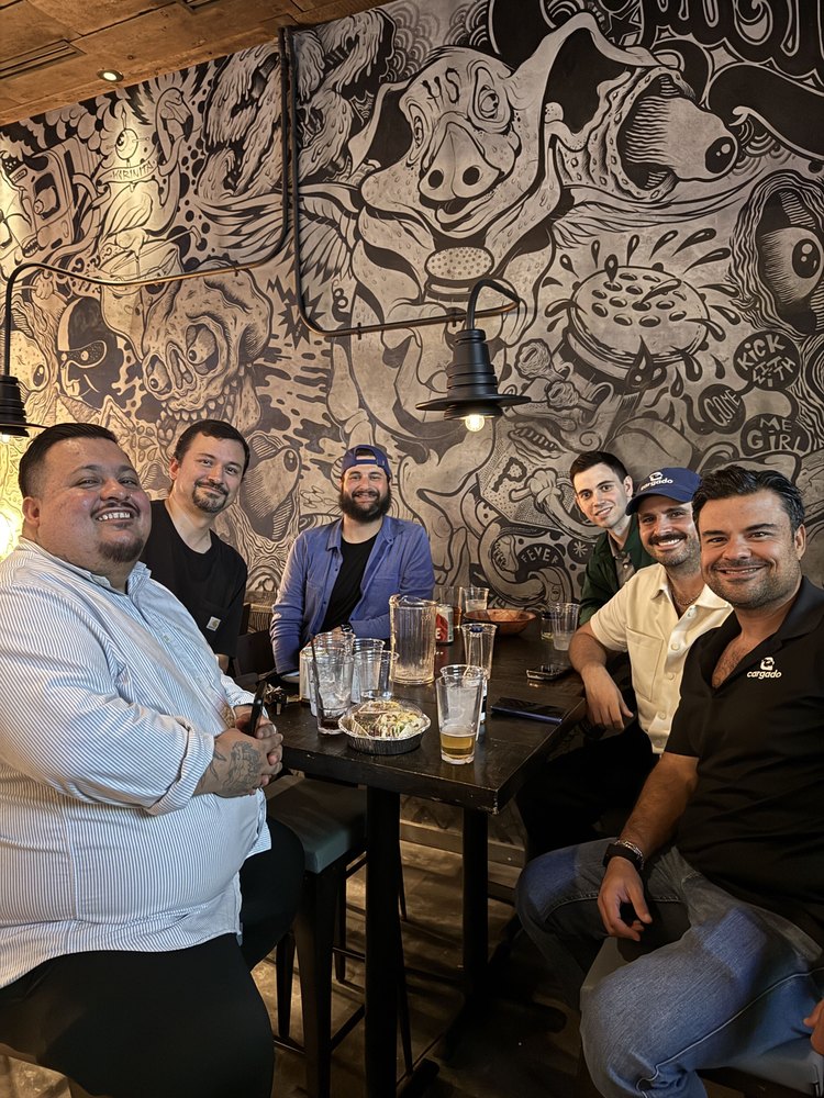Six teammates at a bar table in front of a mural