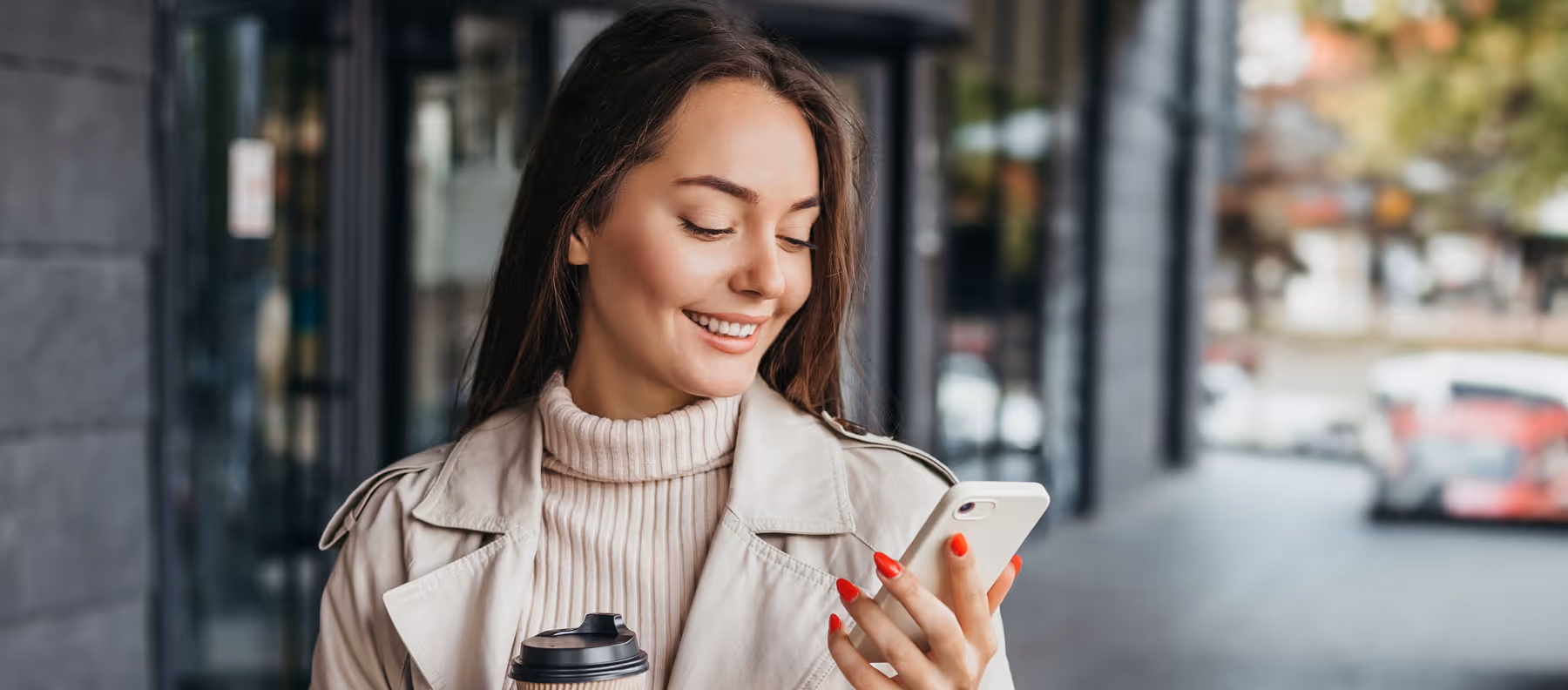 Smiling woman outside on her mobile with a takeaway coffee in hand