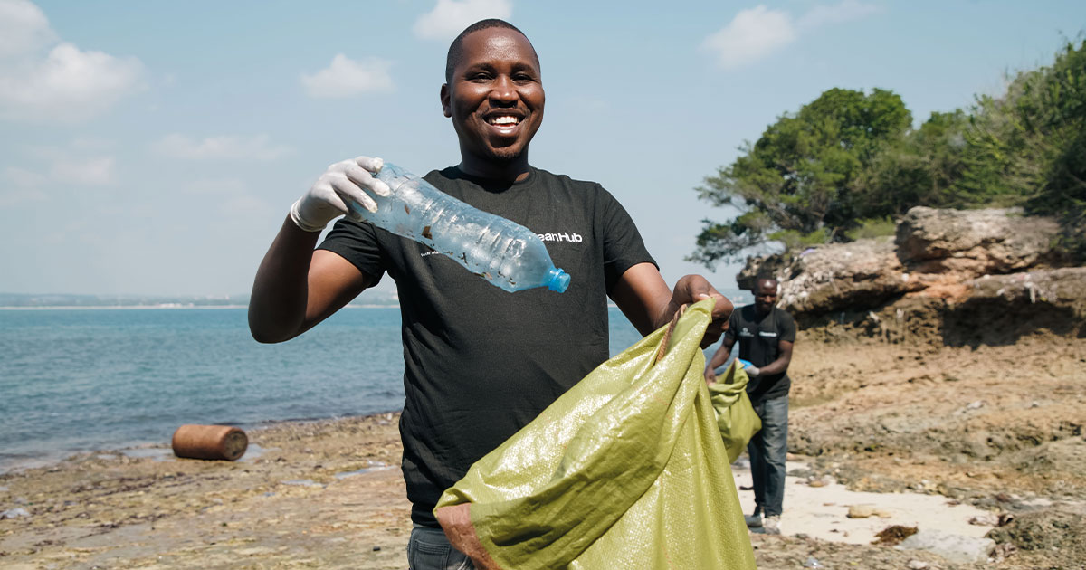 An image of a waste collector smiling at the camera in Dar Es Salaam with a PET bottle in this hand