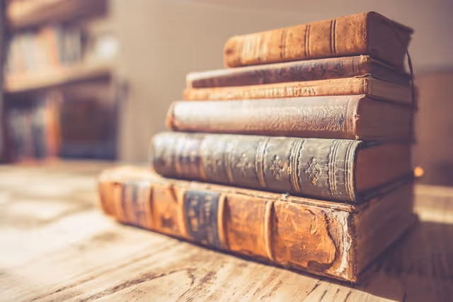 Stack of worn, vintage hardcover books with embossed covers on a wooden table.