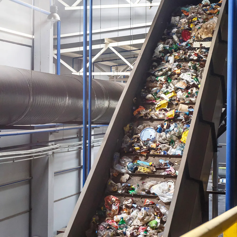 Conveyor belt carrying mixed plastic and paper waste inside a waste processing facility.