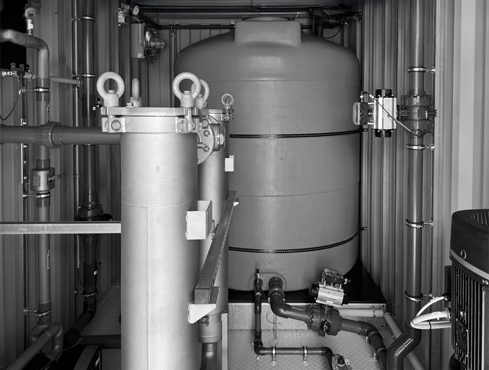 Industrial room with large cylindrical tank, metal pipes, and filtration equipment.