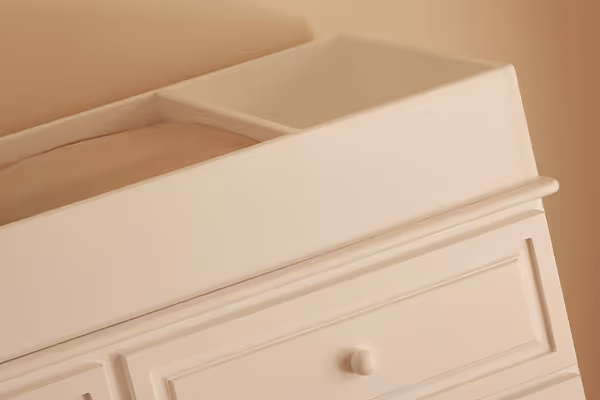 Cambiador beige de madera con cajones y bordes redondeados en una habitación.