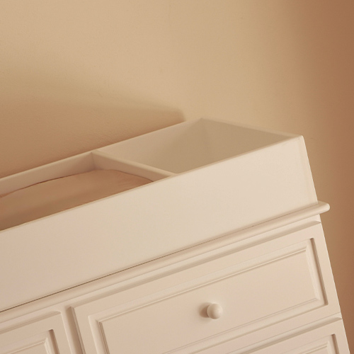 Cambiador blanco sobre una cómoda blanca contra una pared beige.