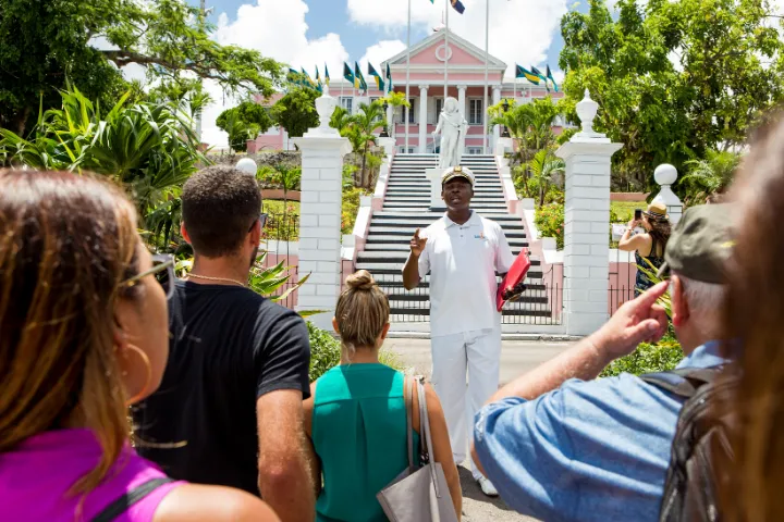 A tour guide speaking to a group of tourists in front of a large pink colonial-style government building with white columns and a statue at the stairs.