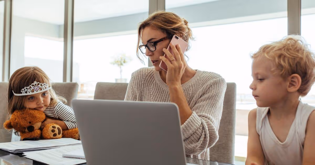 Children sitting next to their morther while she works on the computer and talks on the phone