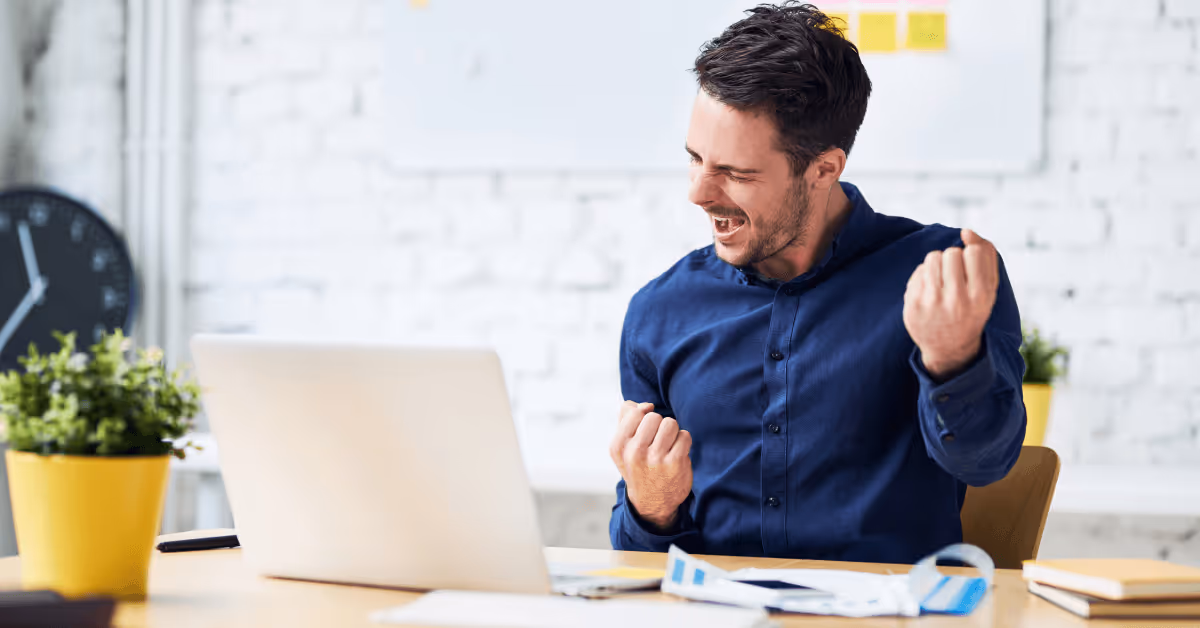 Developer in front of laptop with blue dress shirt celebrating success