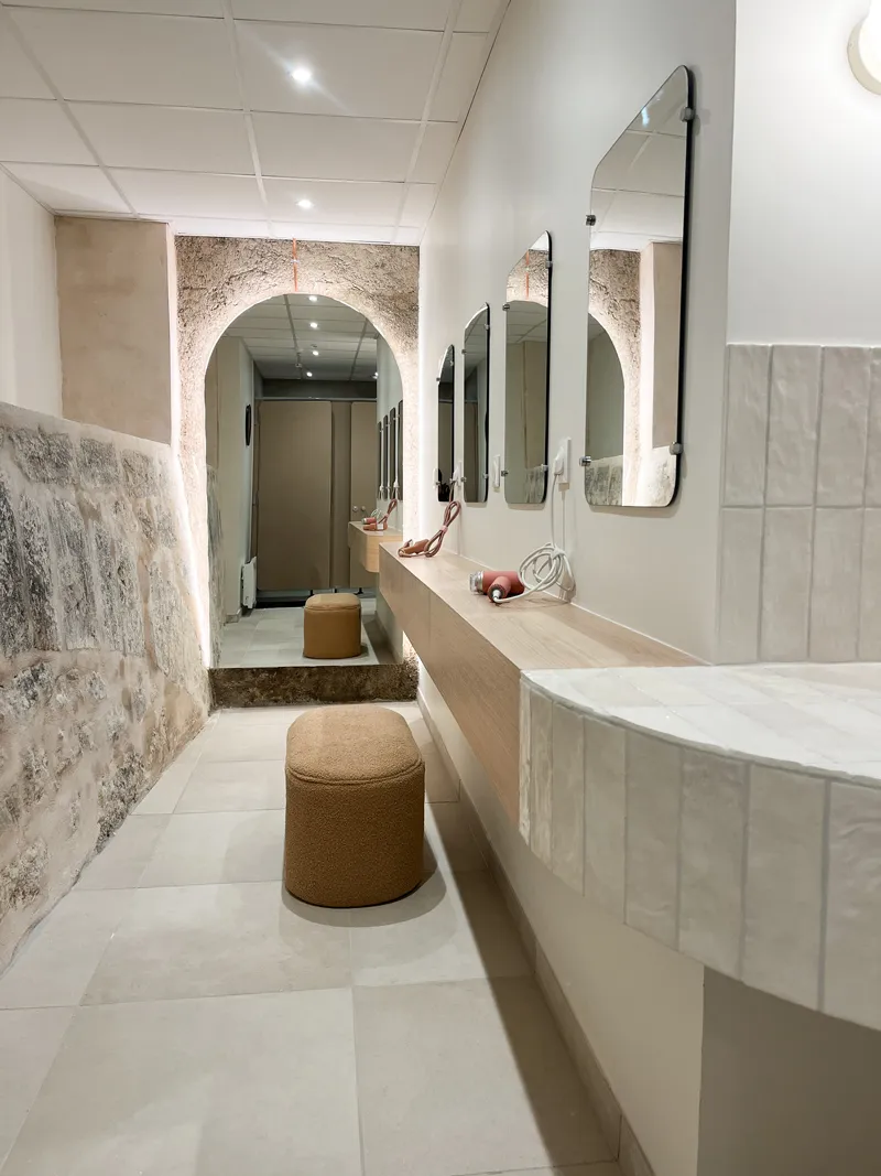 Couloir lumineux avec banquette beige, miroirs suspendus et mur en pierre avec arche éclairée.