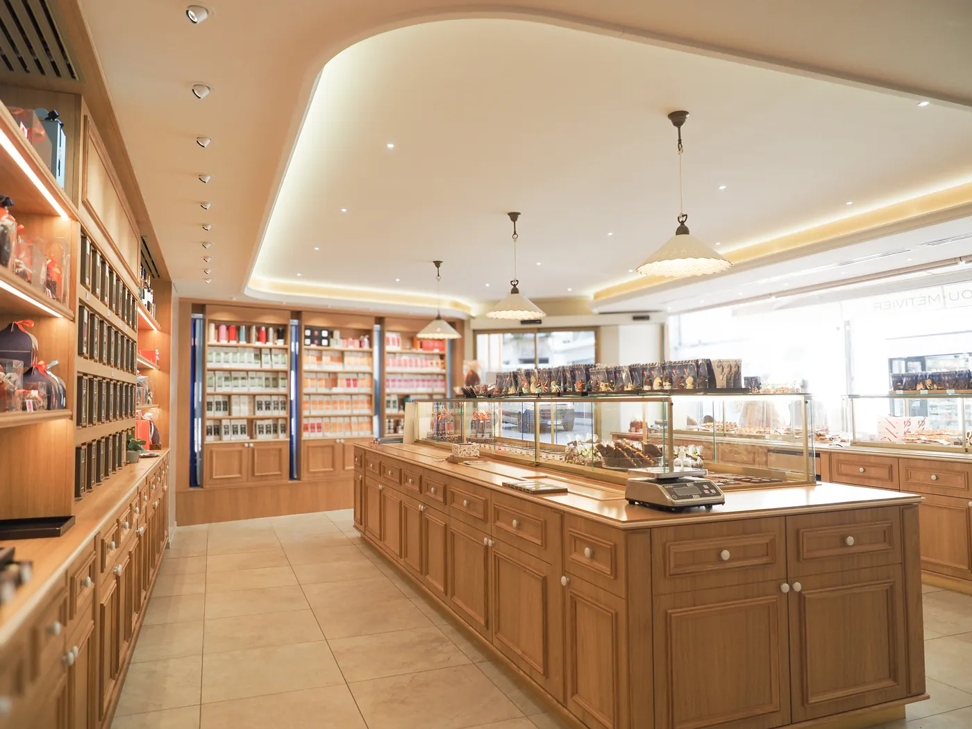 Intérieur lumineux d'une boutique de confiserie avec présentoirs en bois et vitrine réfrigérée remplie de chocolats.