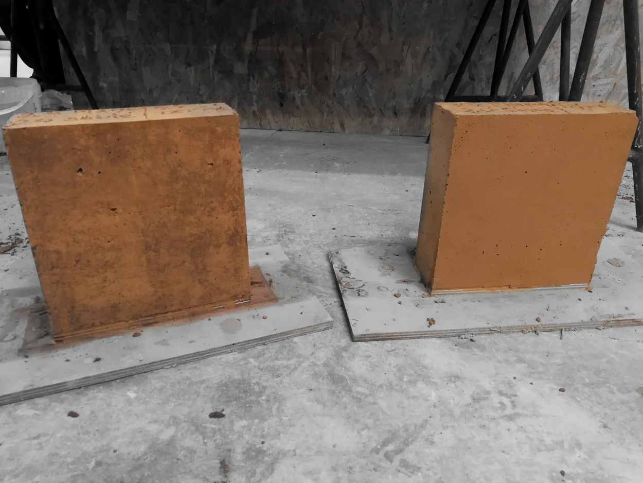 Deux blocs rectangulaires en terre crue cuite posés sur des plaques en bois sur un sol gris.
