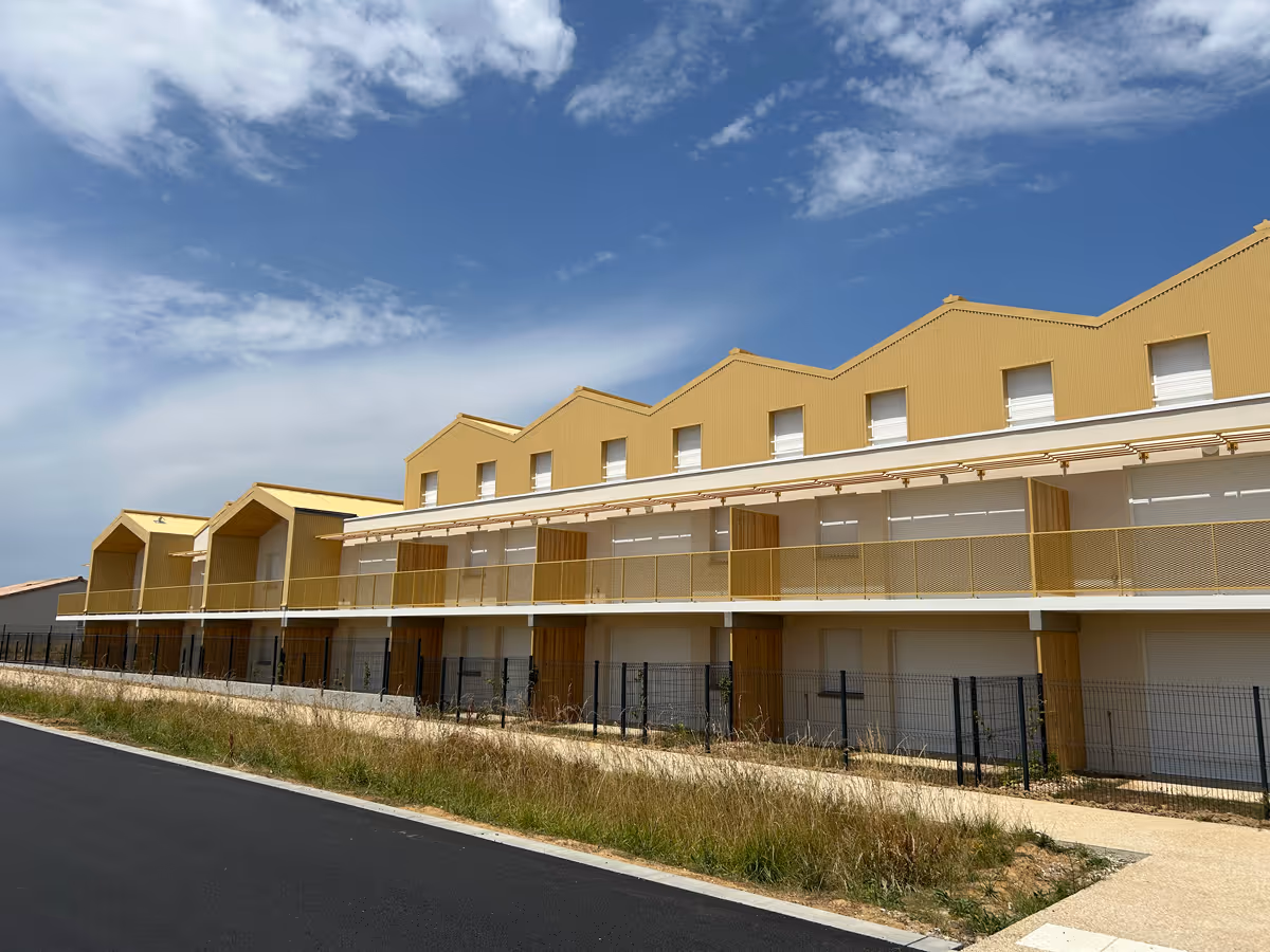 Bâtiment jaune aux multiples toits en pignon sous un ciel bleu partiellement nuageux.