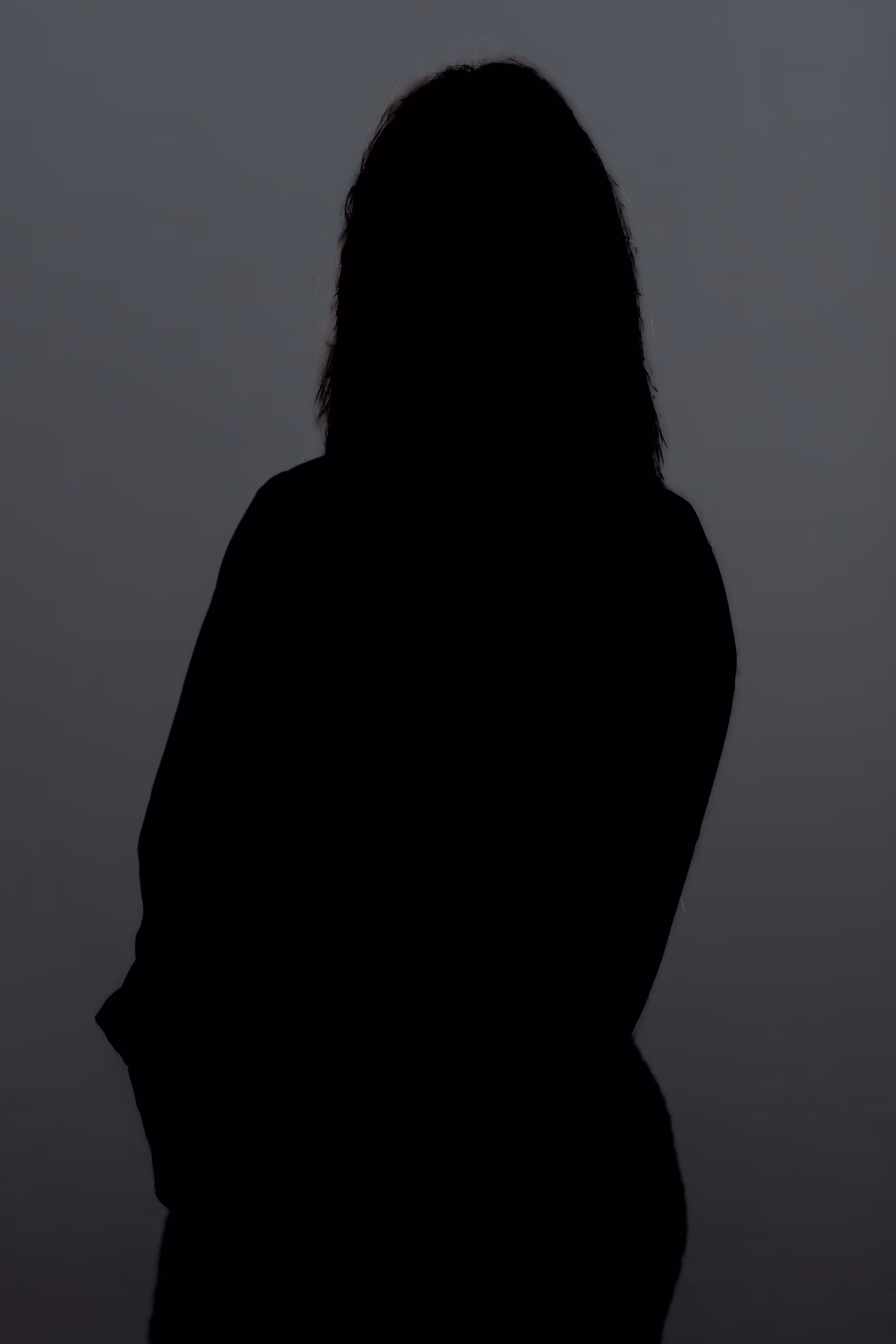 Silhouette d'une personne aux cheveux mi-longs debout face à un fond gris.