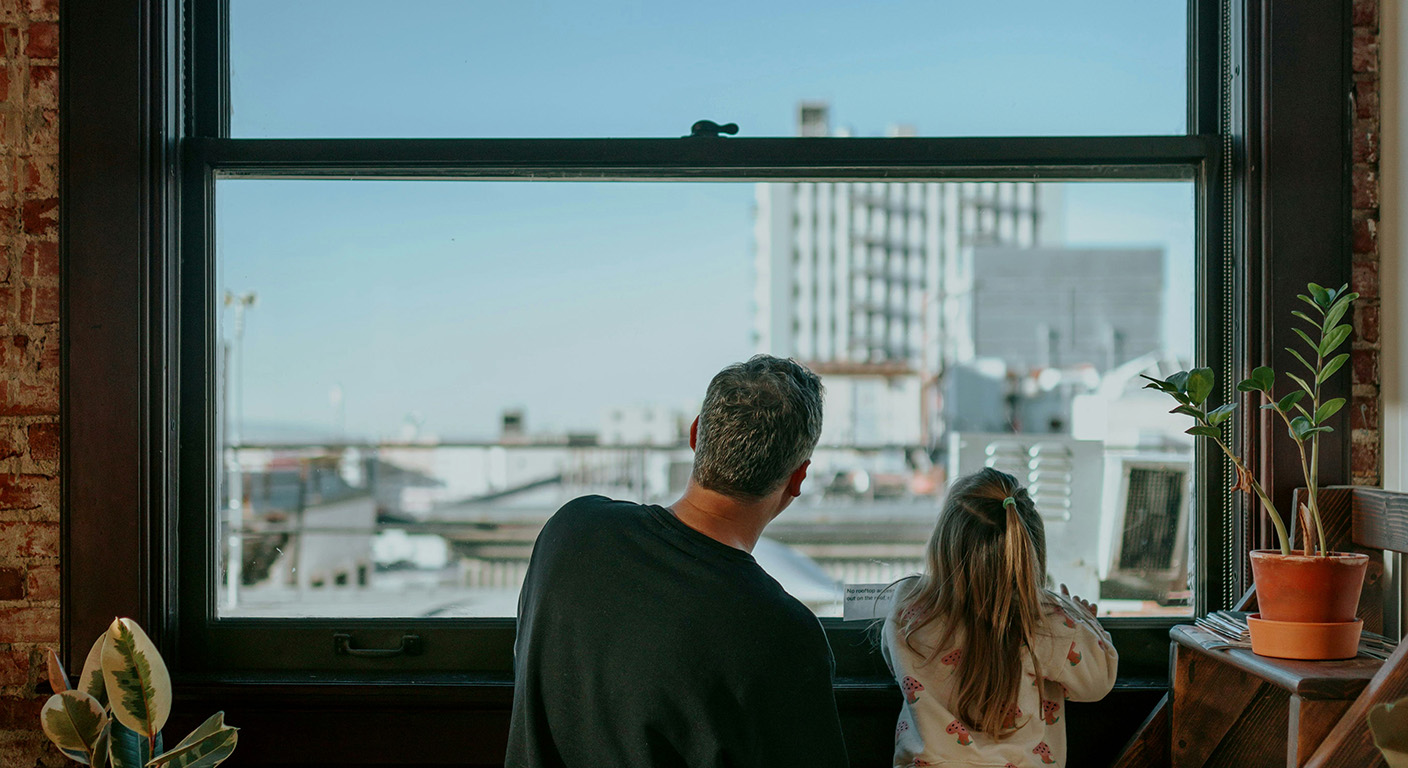 Small business owner looking out the window with young daughter