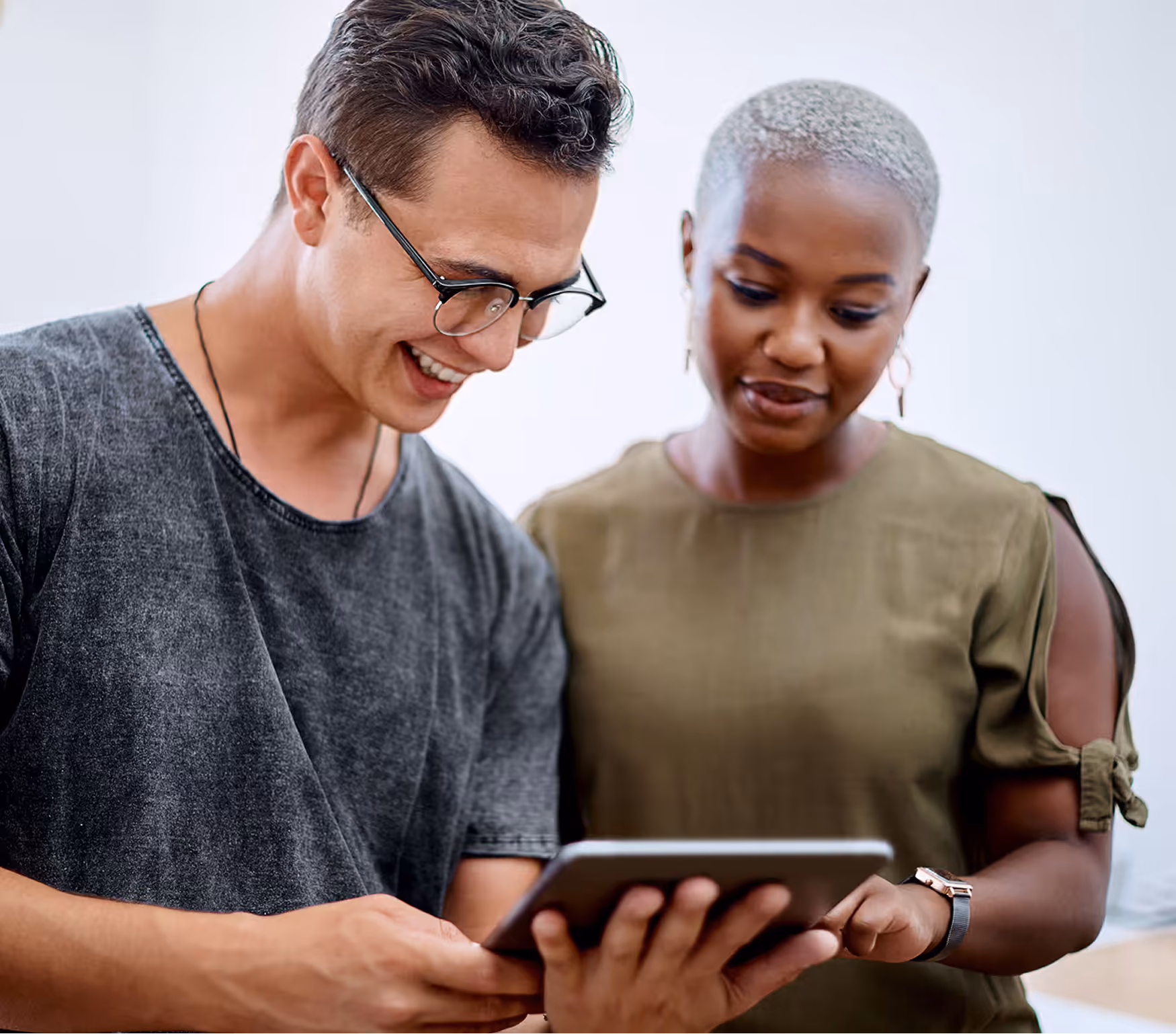 Two people smiling and looking at a tablet together indoors.