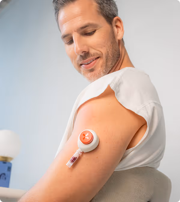 Man with rolled-up sleeve looking at a small blood collection device on his upper arm.