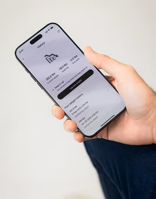 Hand holding a smartphone showing weight history and current weight tracking app screen.