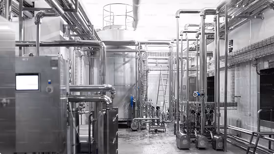 Industrial room with metal pipes, valves, pumps, and a control panel with a digital display.