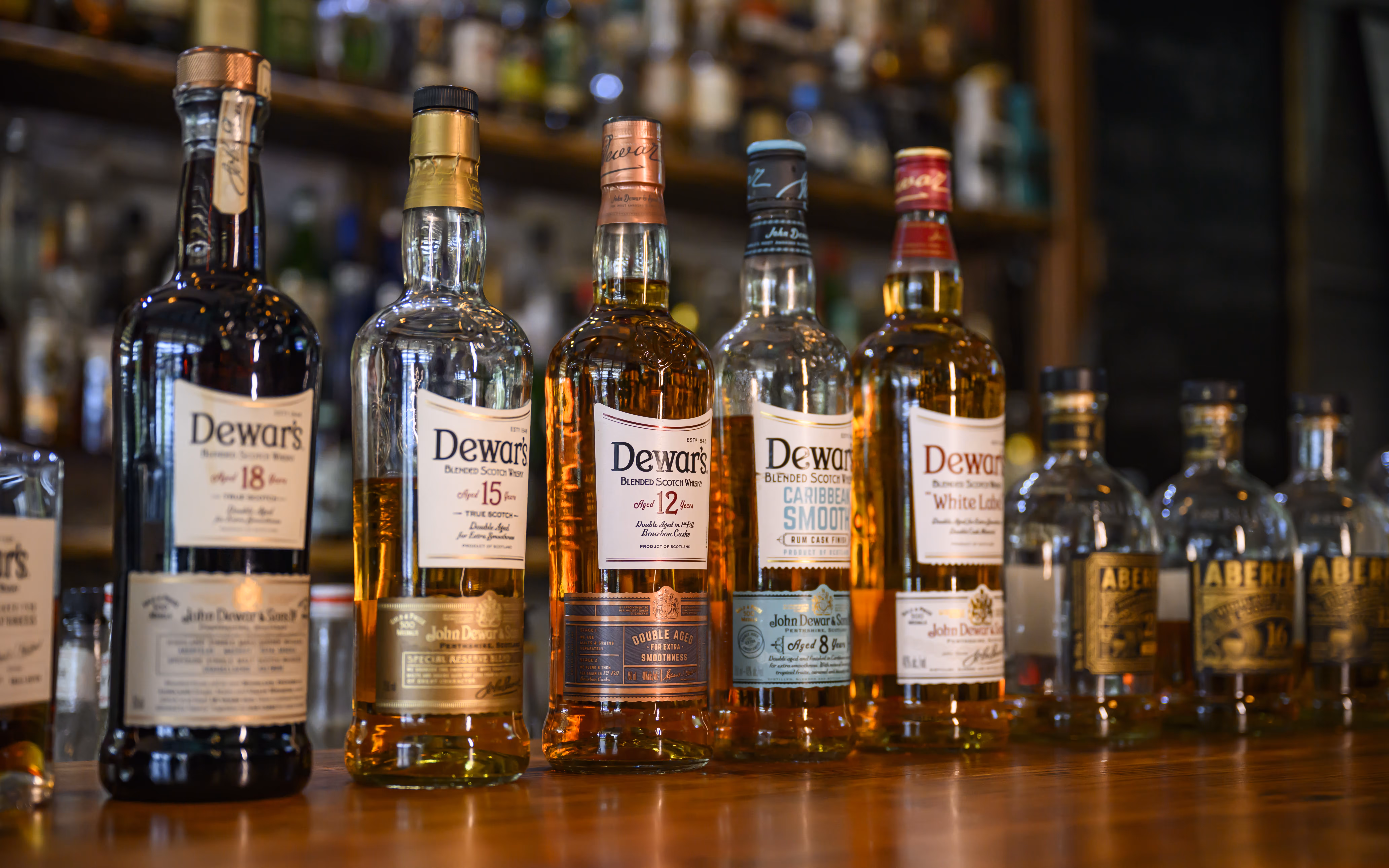 Row of Dewar's blended Scotch whisky bottles on a wooden bar counter.