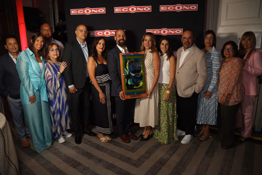 Group of people standing together indoors in front of a black backdrop with 'ECONO' logos, with a man and woman in the center holding a colorful framed artwork.