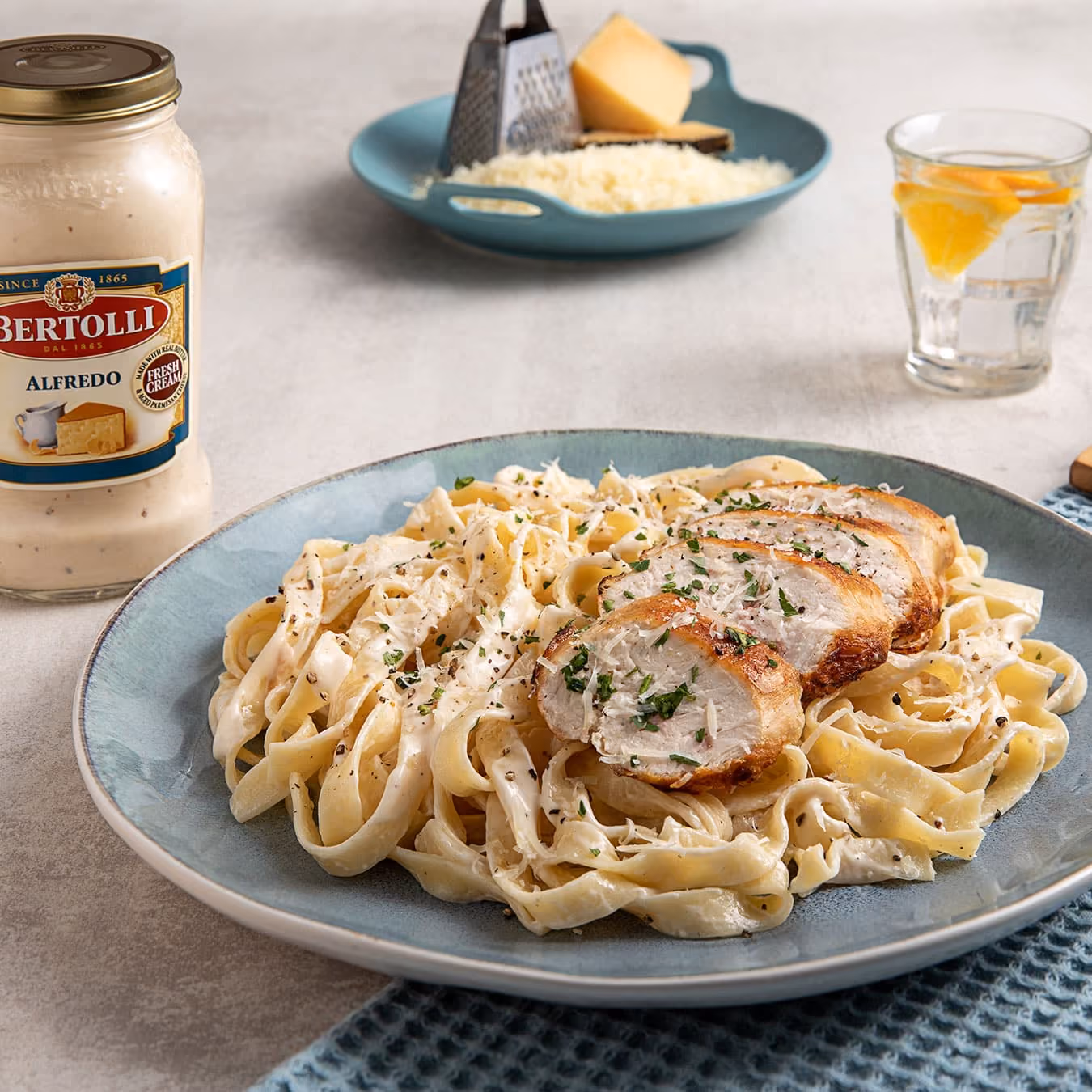 Plate of chicken fettuccine Alfredo garnished with parsley and grated cheese, next to Alfredo sauce jar.
