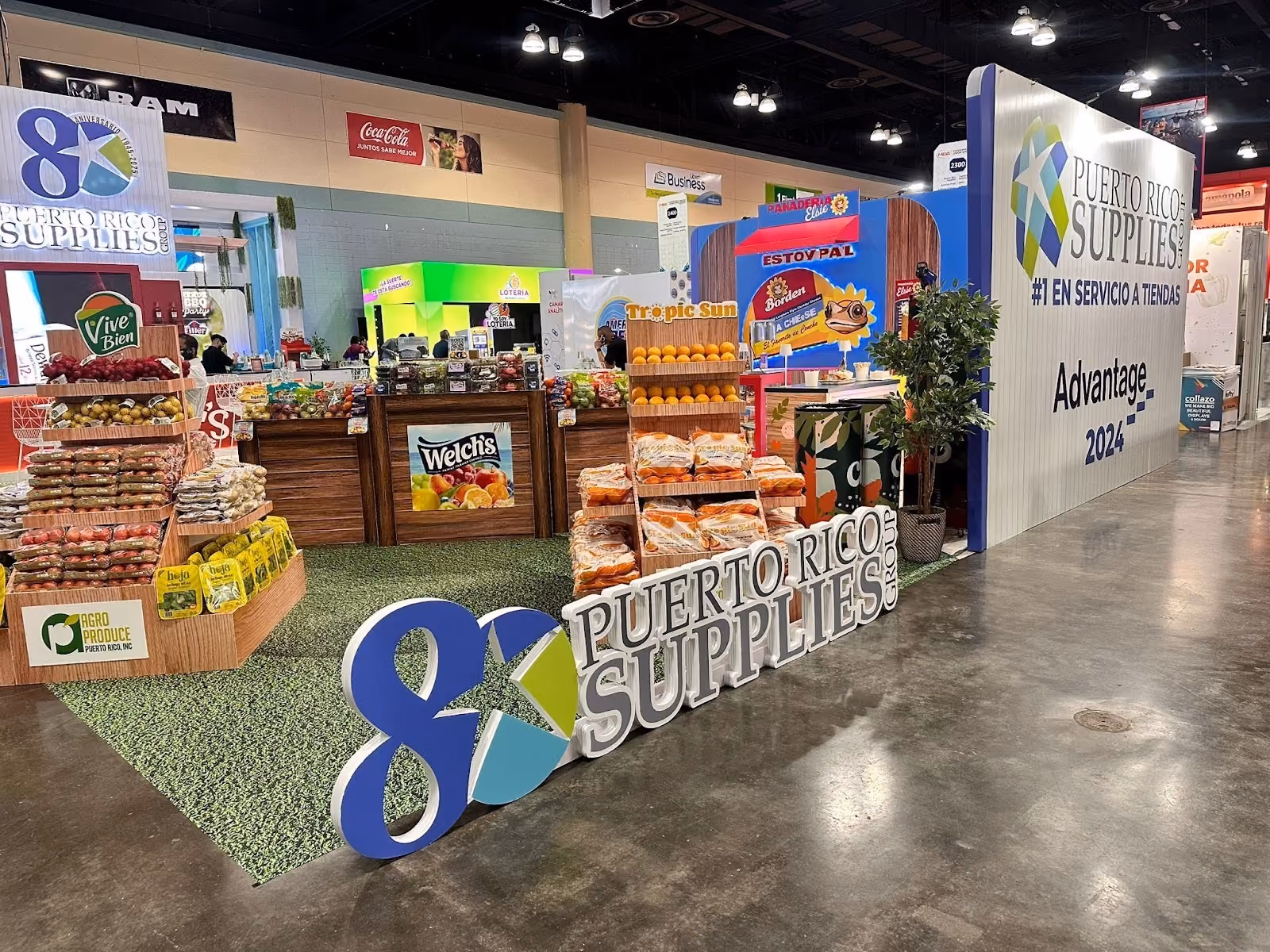 Exhibit booth with Puerto Rico Supplies Group sign and displays of fruits and packaged goods at a trade show.