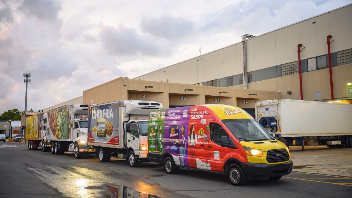 Colorful delivery trucks lined up outside a warehouse under a cloudy sky at dusk.