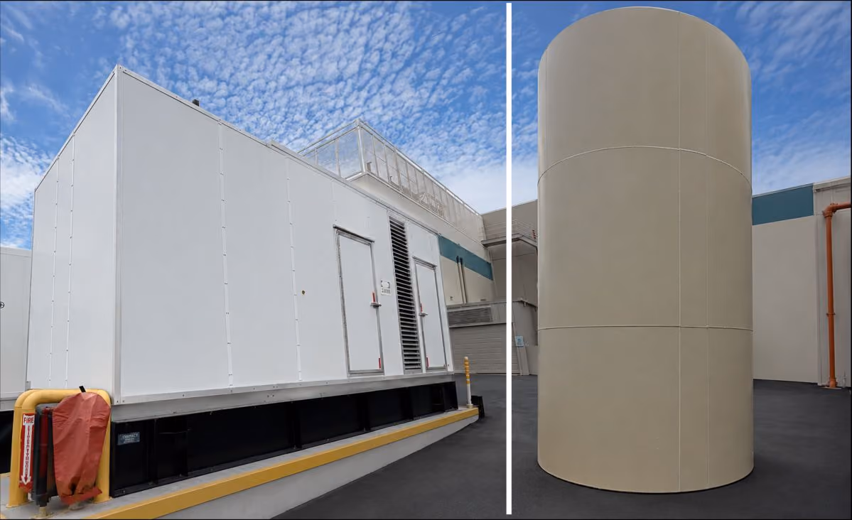 Large white industrial generator and tall beige cylindrical tank outside a building under a blue sky.
