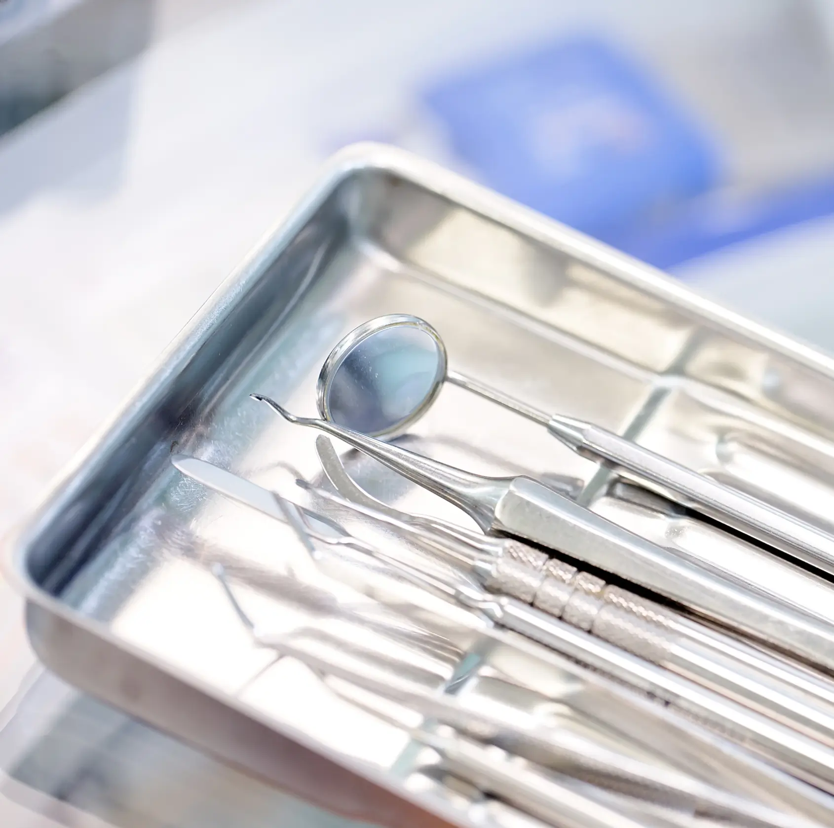 Close-up of stainless steel dental instruments, including a dental mirror and scalers, arranged in a metal tray.