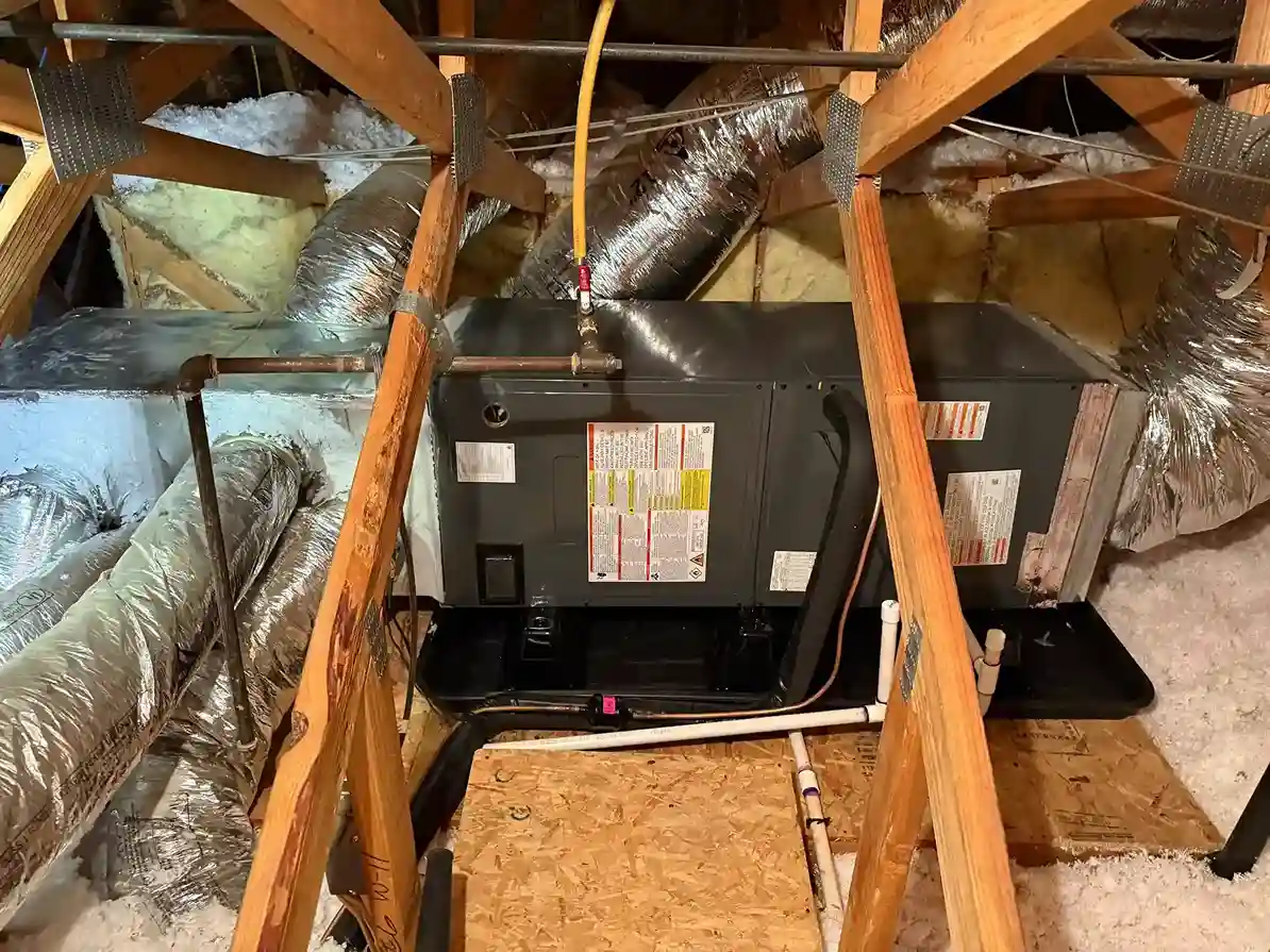 Air handler unit in attic space with ductwork and insulation.