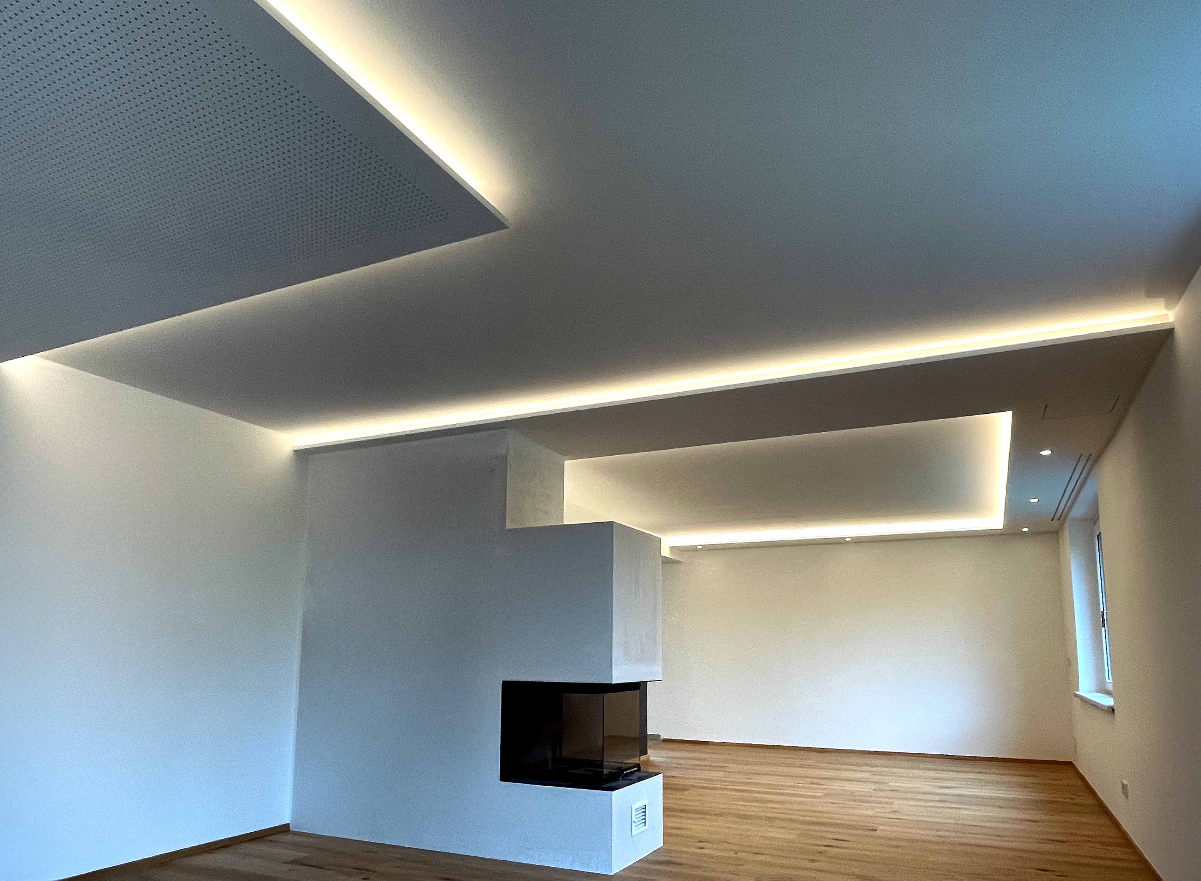 Moderner, leerer Wohnraum mit hellen Holzböden, weißem Kamin und indirekter LED-Deckenbeleuchtung.