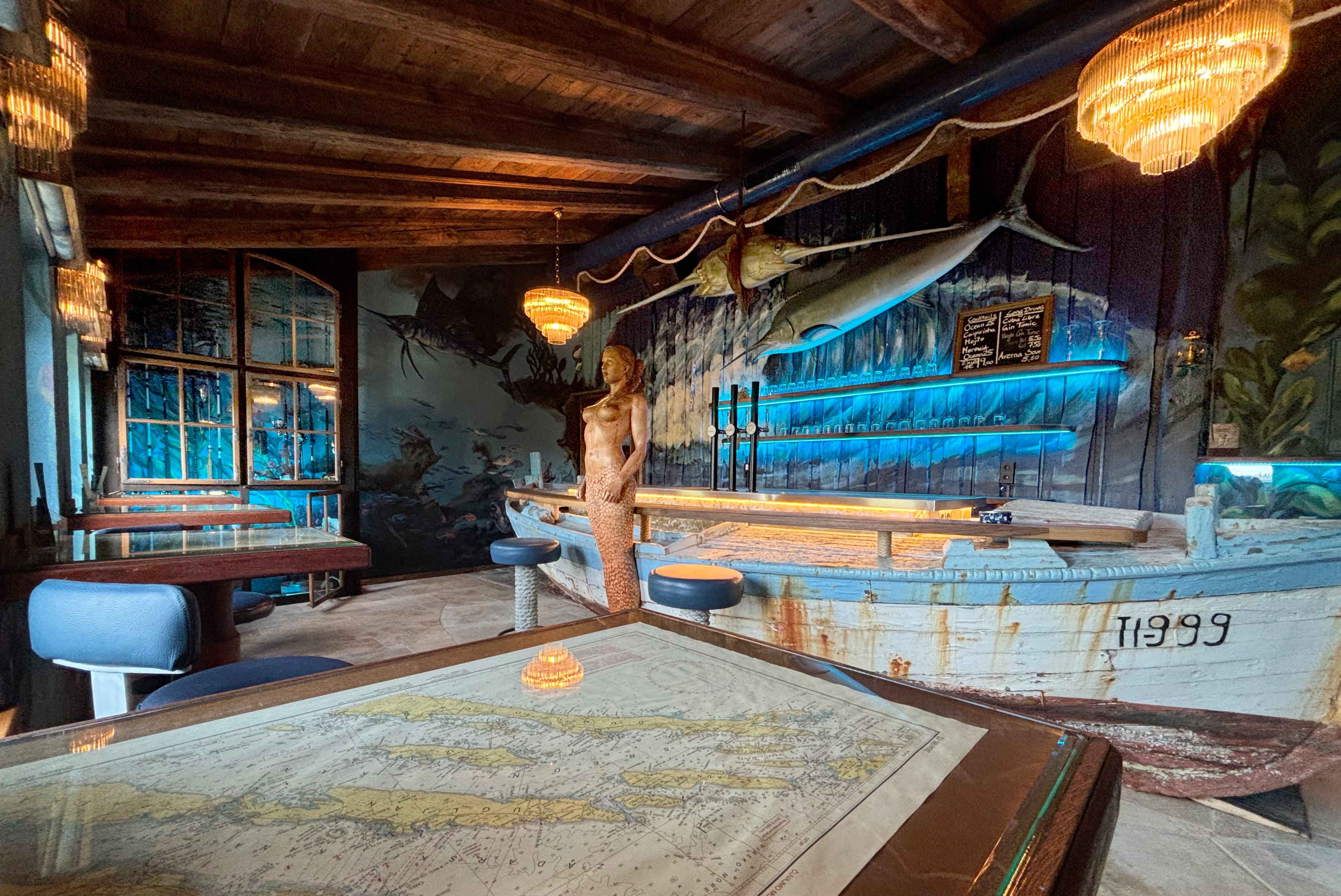 Bar im maritimen Stil mit Holzboot als Theke, Meerjungfrau-Statue und Wanddekorationen mit Fischen.