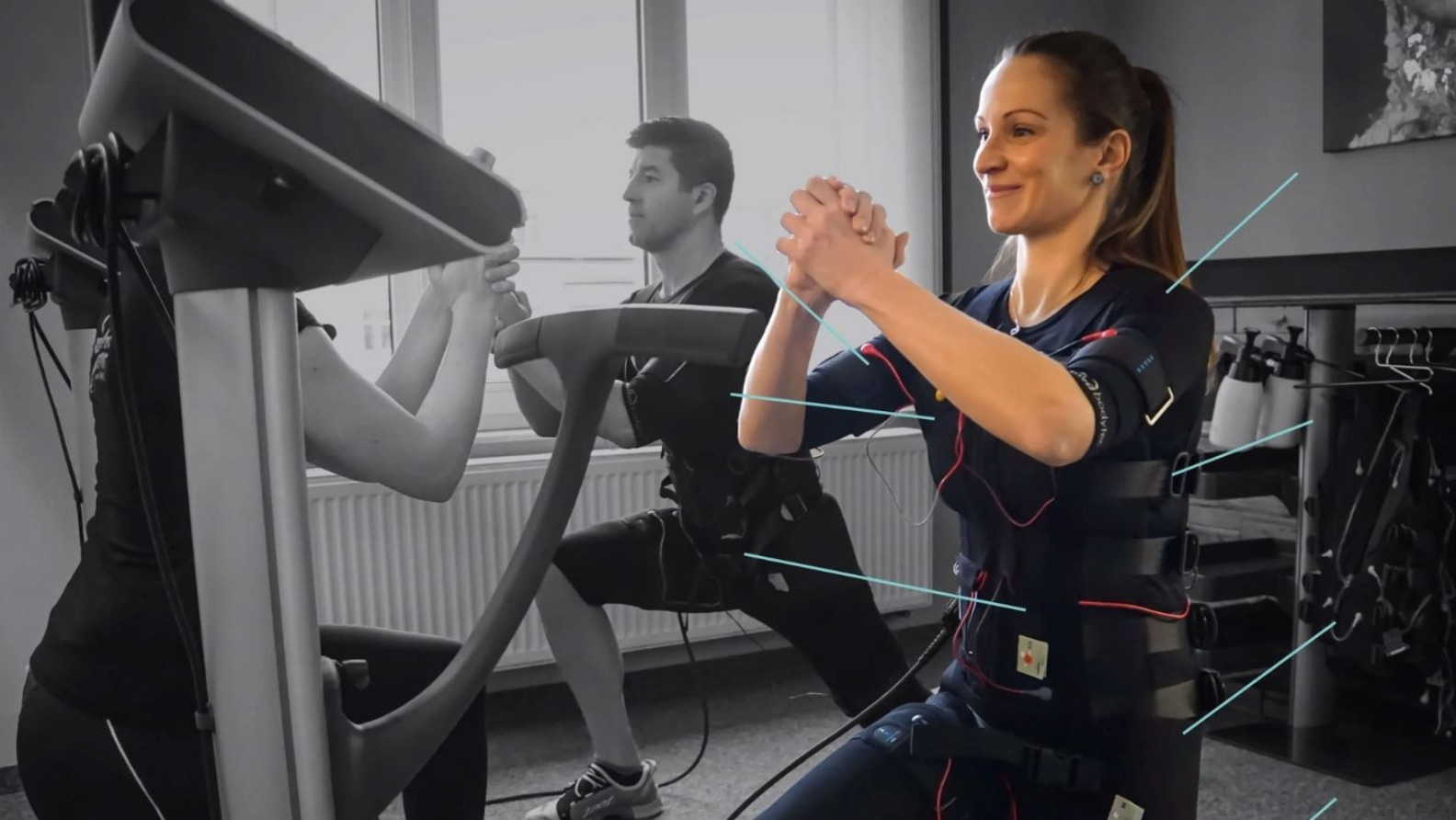 Frau beim EMS-Training im MyMove Fitness Glattbrugg mit elektrischer Muskelstimulation und Personal Trainer im Hintergrund